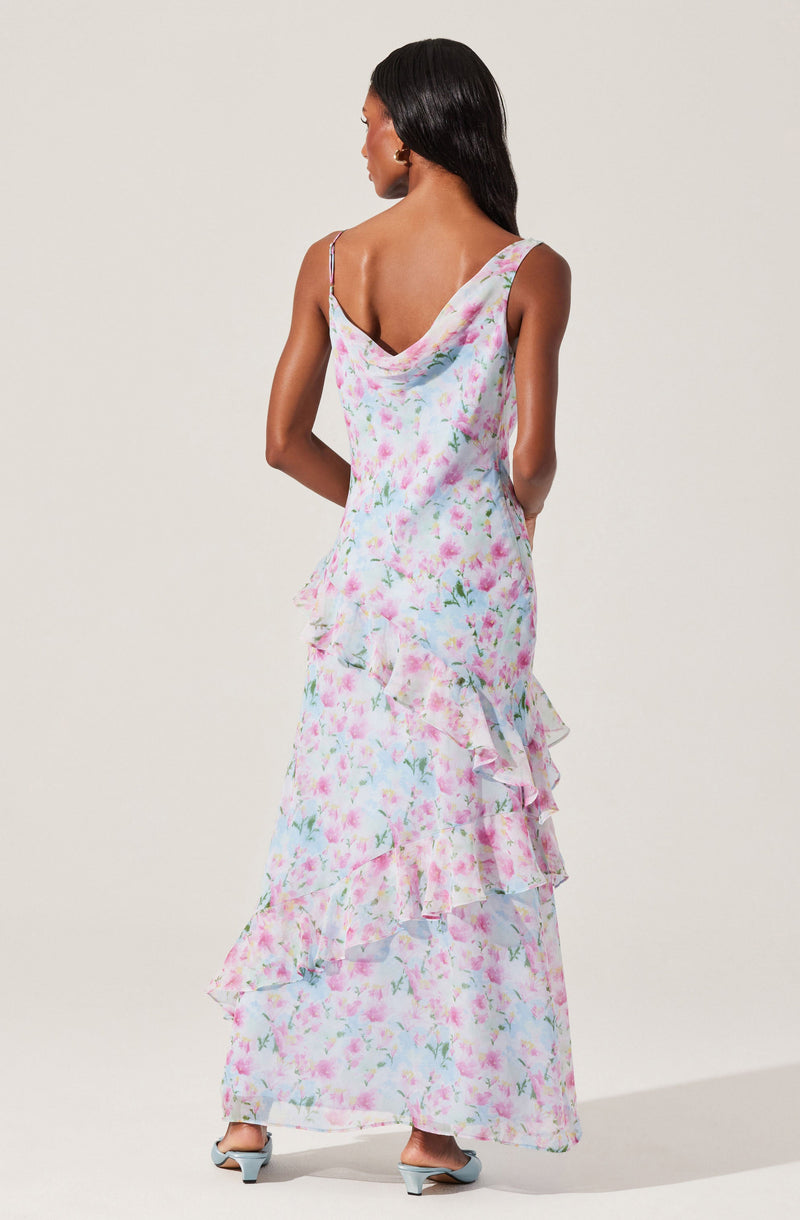A woman is wearing a long, sleeveless dress with a floral pattern in soft pastel colors. The dress features thin spaghetti straps, a relaxed draped neckline, and a tiered, ruffled skirt that reaches the floor. The fabric appears lightweight and flowy.