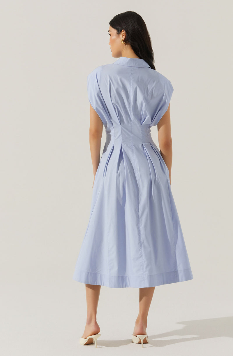 A woman is wearing a light blue, sleeveless, collared dress with a fitted waist and a flared, midi-length skirt. The dress has pleats at the waistline, creating a gathered effect, and the fabric appears to be lightweight with a subtle sheen. She is also wearing white heeled shoes.