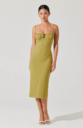 A woman is wearing a lime green, textured, fitted midi dress with spaghetti straps. The dress features a gathered bust area with a small cutout in the center. She is also wearing open-toed, beige high-heeled sandals and small earrings.