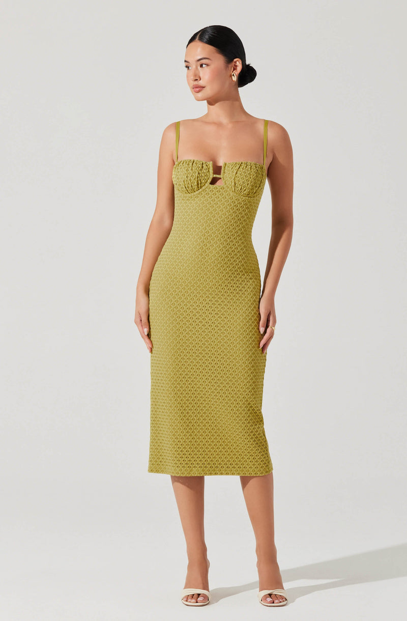 A woman wearing a sleeveless, midi-length, fitted dress in a greenish-yellow color. The dress features thin spaghetti straps and a textured, patterned fabric. The bust area has a ruched design with a small cut-out in the center.