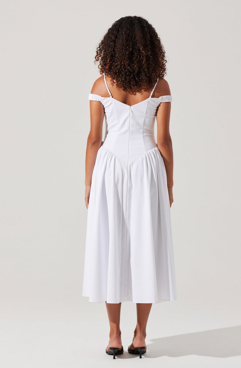 A woman wearing a white, off-the-shoulder dress with thin spaghetti straps. The dress features a fitted bodice and a full, gathered skirt that falls below the knees. She is also wearing black, open-toe heels.