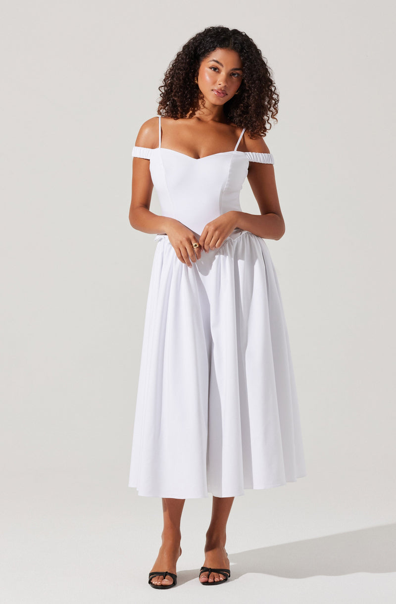 A woman is wearing a white dress with thin spaghetti straps and off-the-shoulder sleeves that have a textured band. The dress has a fitted bodice and a high-waisted, wide, pleated skirt that falls to mid-calf length. She is also wearing black open-toe sandals with ankle straps.