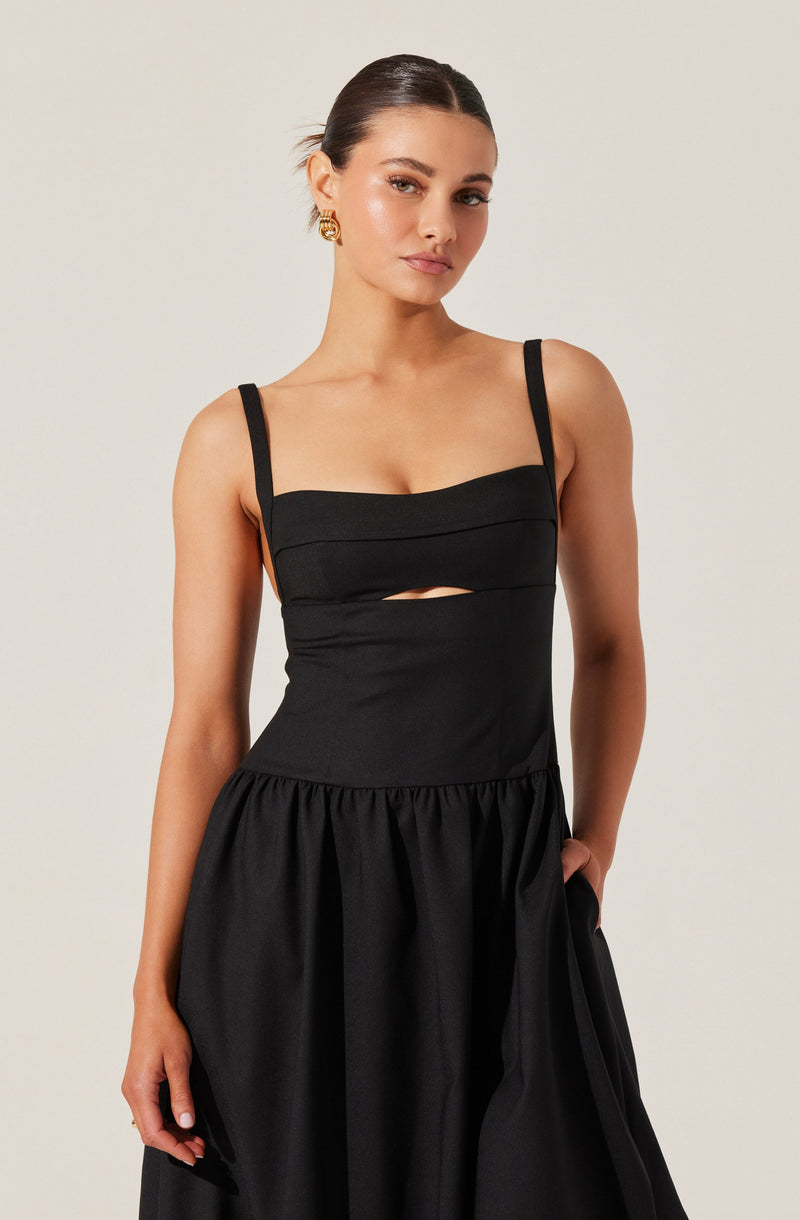 The woman is wearing a black sleeveless dress with thin straps. The bodice features horizontal seam details and a small cut-out detail just below the bust. The skirt of the dress is gathered at the waist, creating a voluminous and flowing appearance.