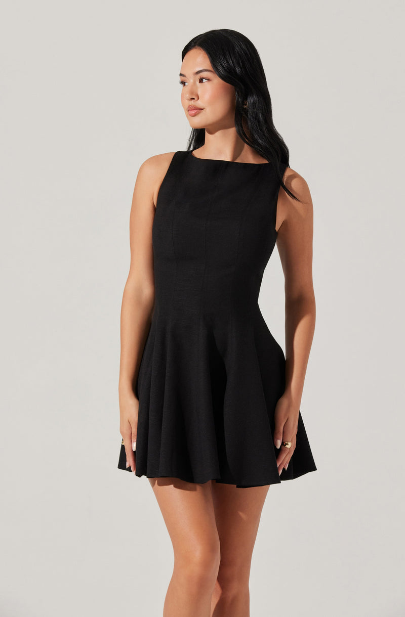 A woman is wearing a sleeveless black dress with a fitted bodice and a flared, pleated skirt. The dress has a round neckline and a subtle sheen, giving it an elegant appearance.