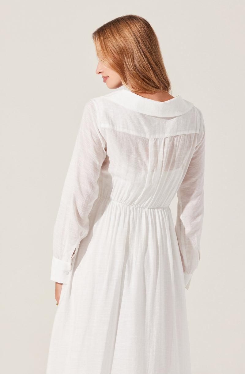 A woman is wearing a long, white dress with a gathered waist and long sleeves. The dress features a collar and appears to be made of a lightweight, semi-sheer fabric.