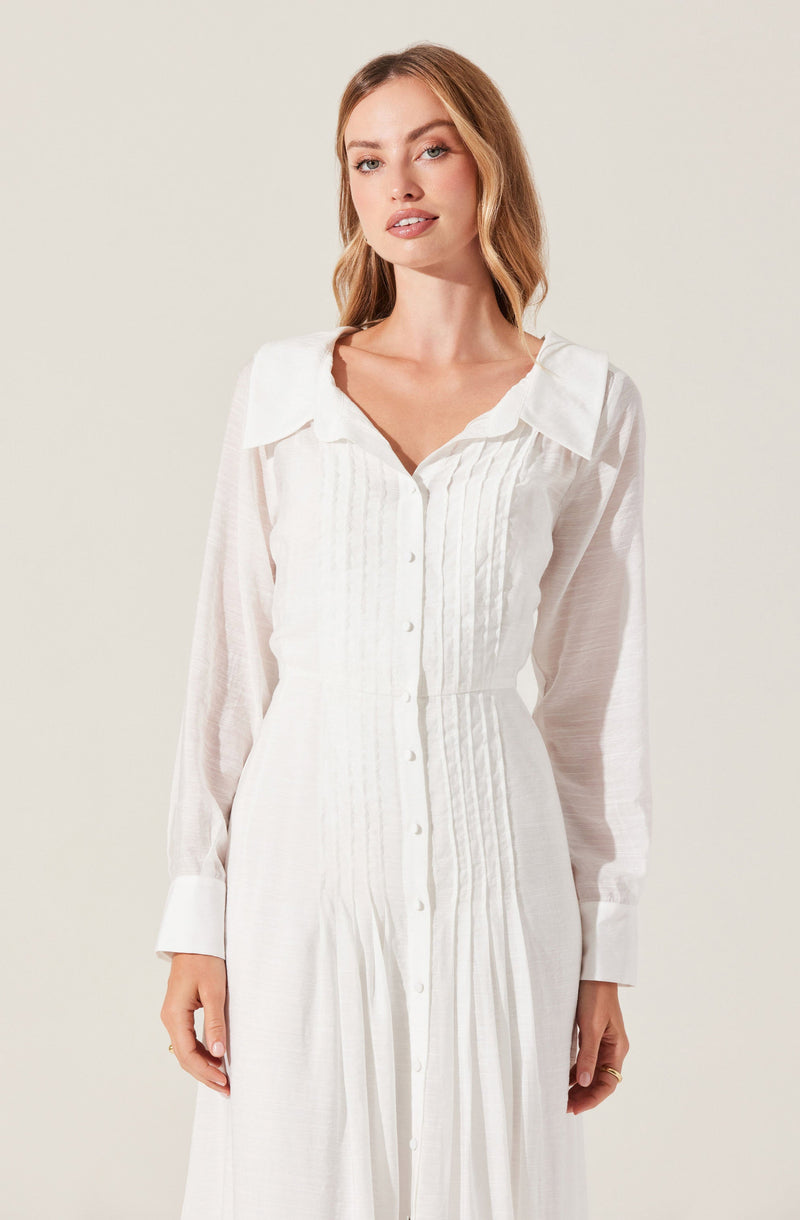 A woman is wearing a long, white, button-down dress with a collar. The dress features vertical pleats along the front and long sheer sleeves with wide cuffs.