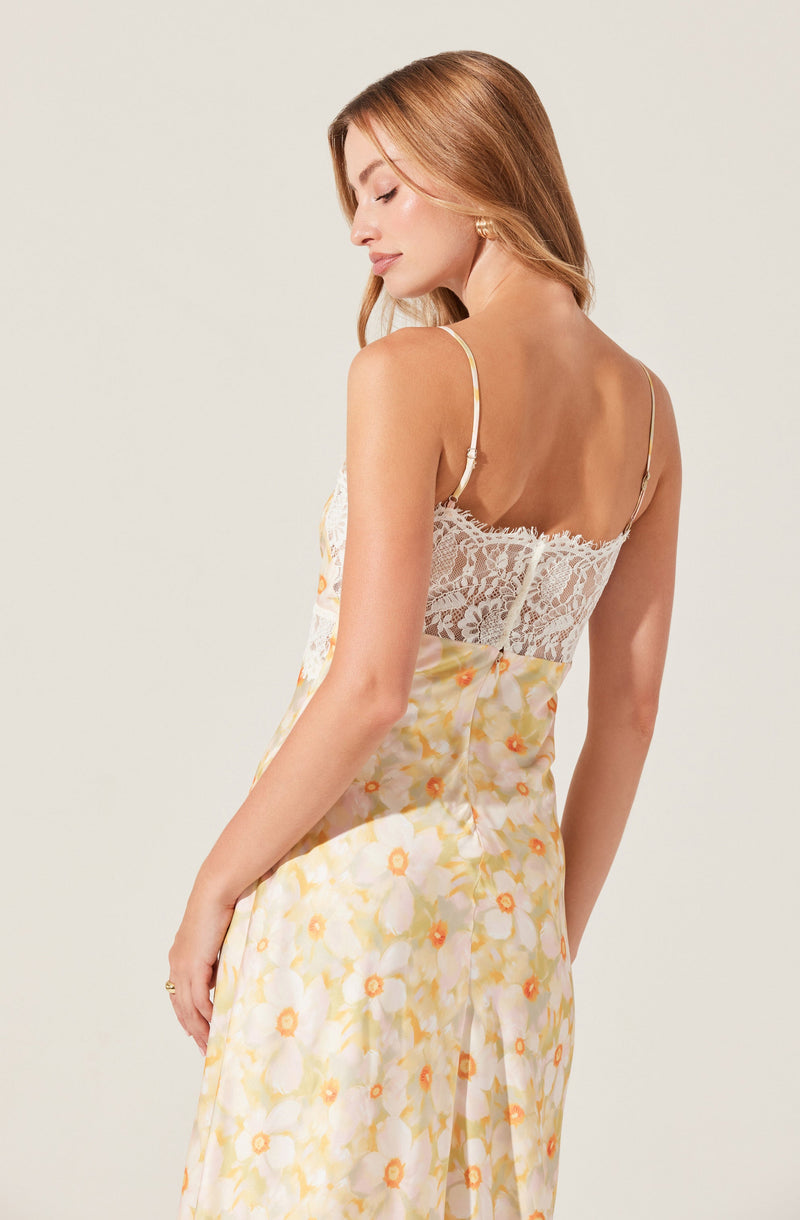 A woman is wearing a spaghetti strap dress featuring a lace back panel and a floral print with yellow, white, and orange flowers.