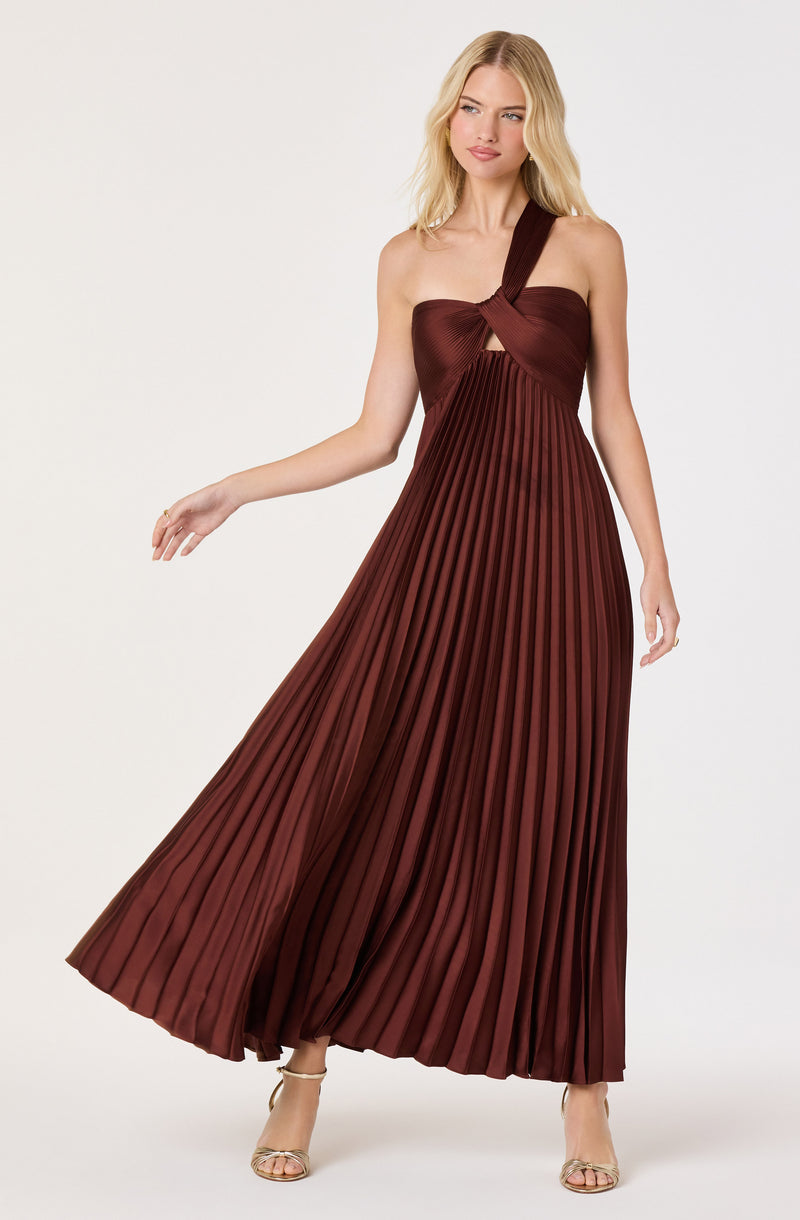 Woman in a burgundy pleated maxi dress with one strap twisted into a knot at the shoulder.