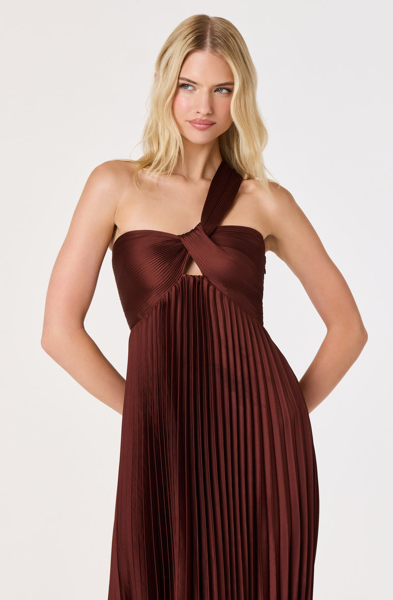 Woman in a sleeveless, brown pleated dress with a twisted bodice and shoulder strap.