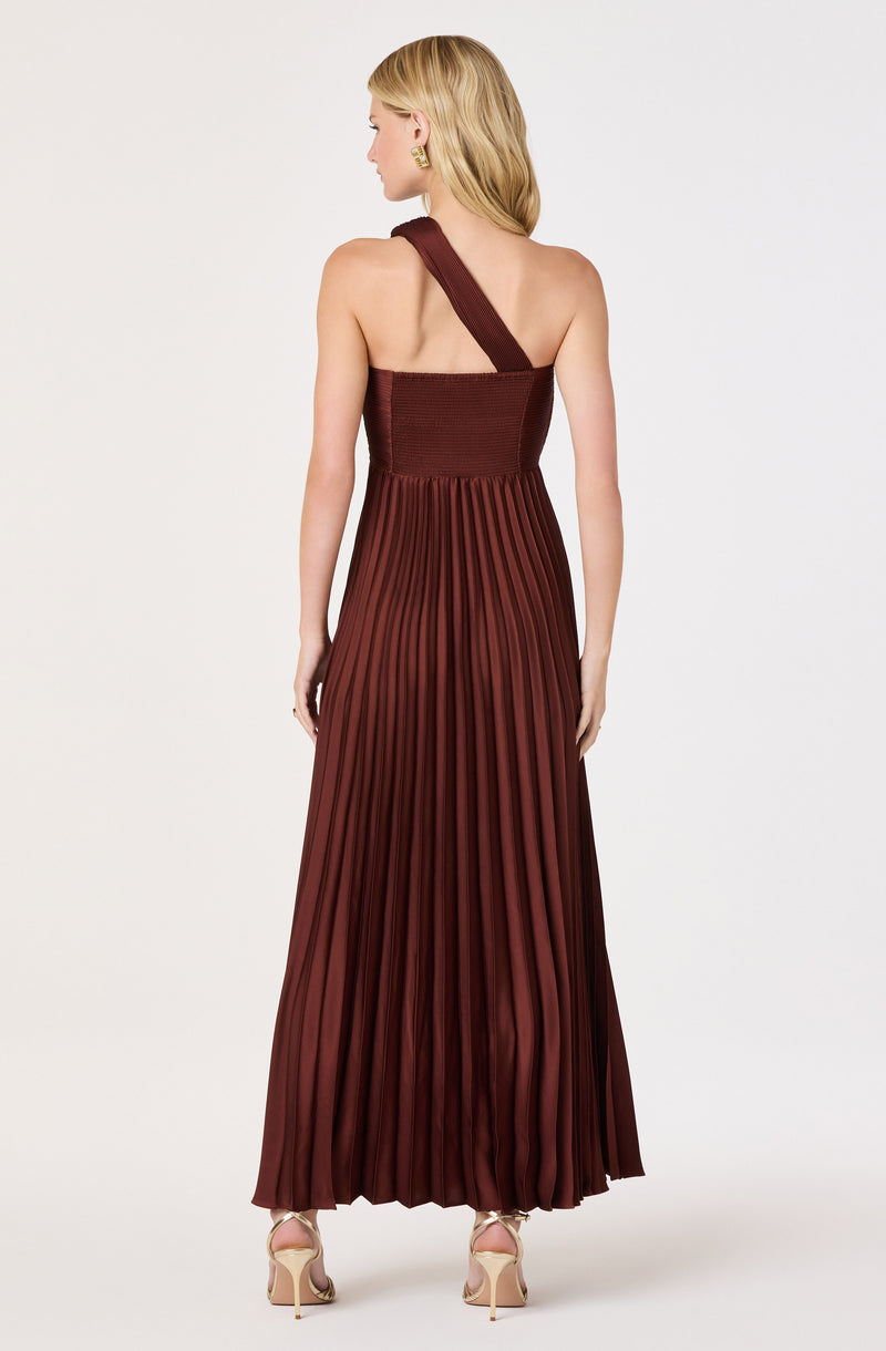 Woman in a burgundy pleated, one-shoulder gown with a strap across her back, wearing gold heels.