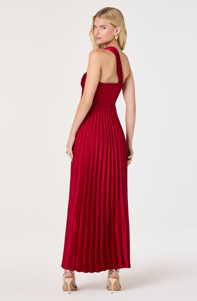Woman in a red sleeveless pleated maxi dress with wide straps, paired with nude heels.
