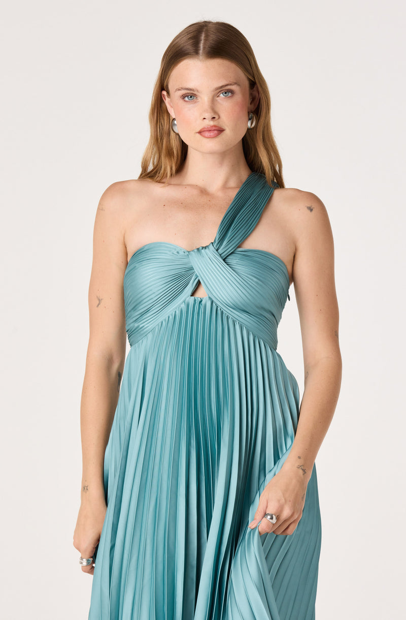 Woman wearing a light blue pleated dress with a twisted strap design on a white background.