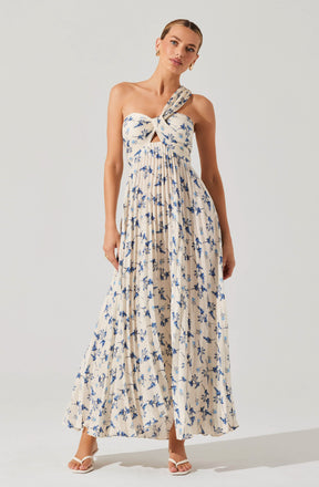 A woman is wearing a sleeveless, long maxi dress with a light beige background and a blue floral print. The dress has a distinctive twisted knot detail at the bust with a small keyhole opening just below it. The skirt is flowing and pleated, creating a soft, airy silhouette.