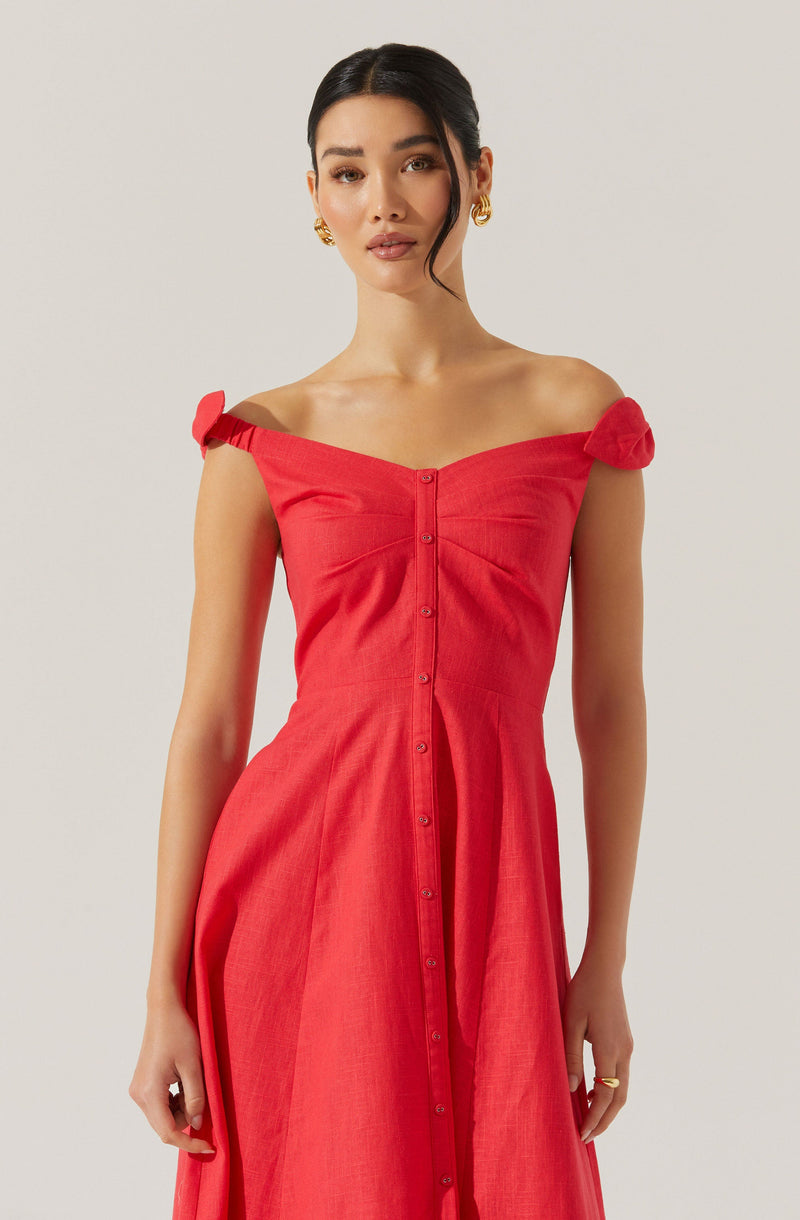 A woman is wearing a bright red, off-the-shoulder dress with short, tied sleeves. The dress has a fitted bodice with vertical seam details and buttons running down the front. The fabric appears lightweight with a slight texture.
