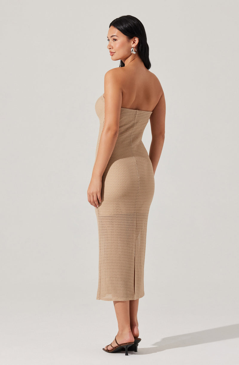 A woman is wearing a strapless, beige, textured, midi-length dress that fits snugly to her body. She has on open-toe, black, heeled sandals with a thin strap across the toes. She accessorized with large, silver, statement earrings.