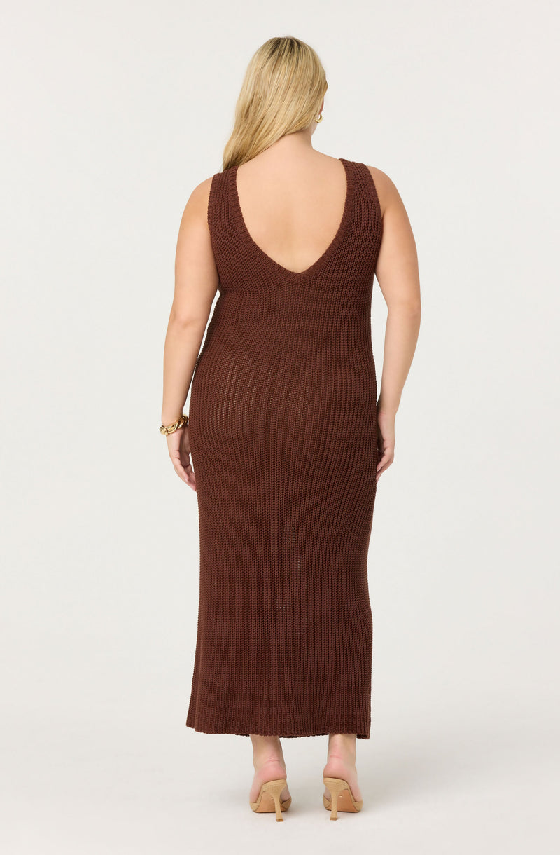 A woman is wearing a sleeveless, ankle-length, knitted dress in a dark brown color. The dress has a deep U-shaped neckline at the back. She is also wearing nude-colored high-heeled shoes and a gold bracelet on her left wrist.