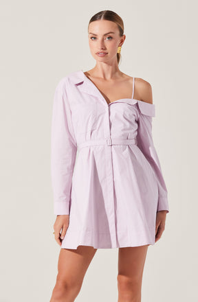 A woman is wearing a light pink, off-the-shoulder shirt dress with long sleeves. The dress features a collar, a front zipper, and a matching belt at the waist. One shoulder is exposed with a thin spaghetti strap, while the other has an oversized, draped sleeve.