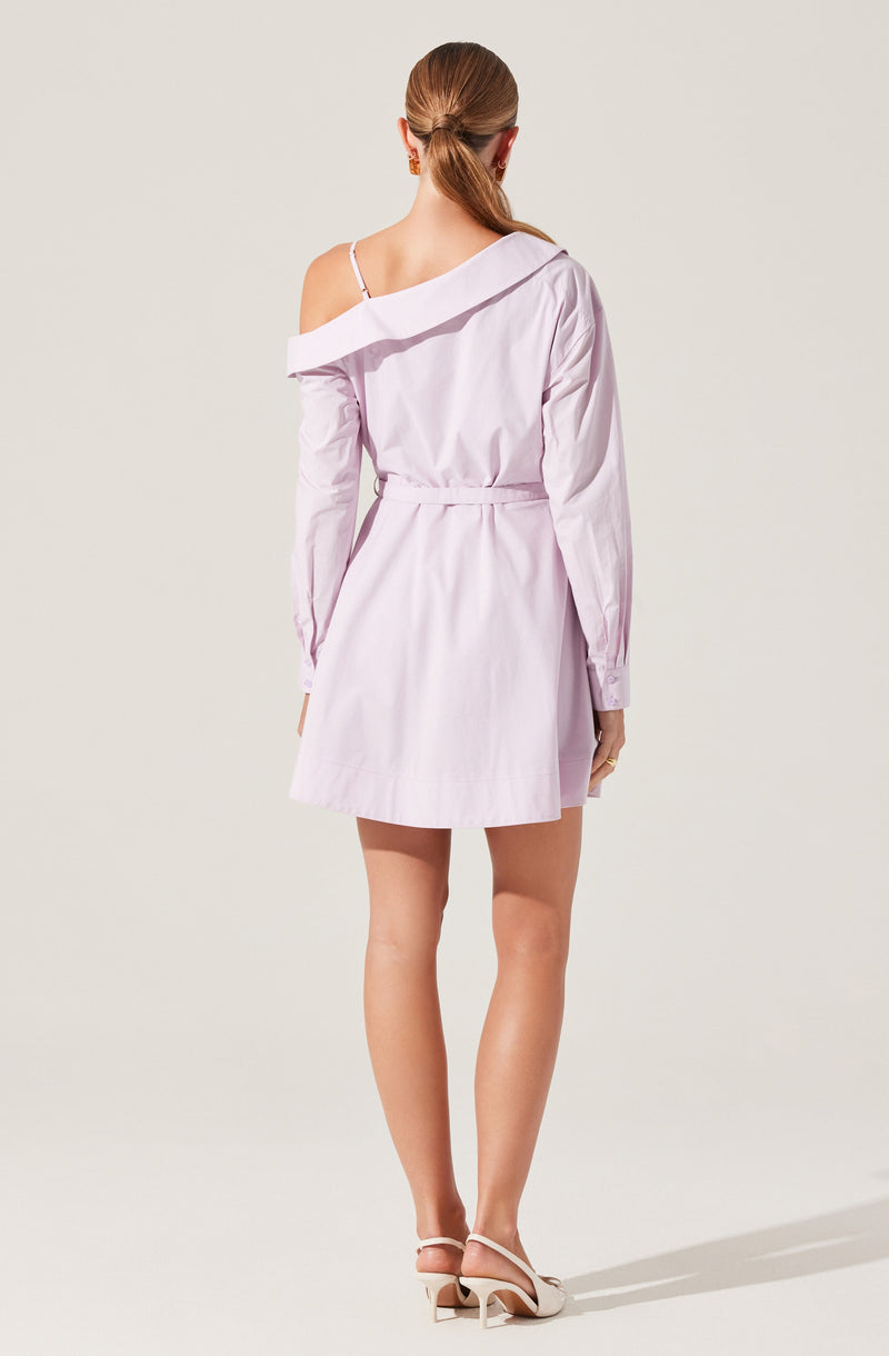 A woman is wearing a light purple, off-the-shoulder shirt dress with long sleeves. The dress has a loose fit with a waist tie and features a single strap detail on her left shoulder. She is also wearing light-colored, open-toe high heels with ankle straps.