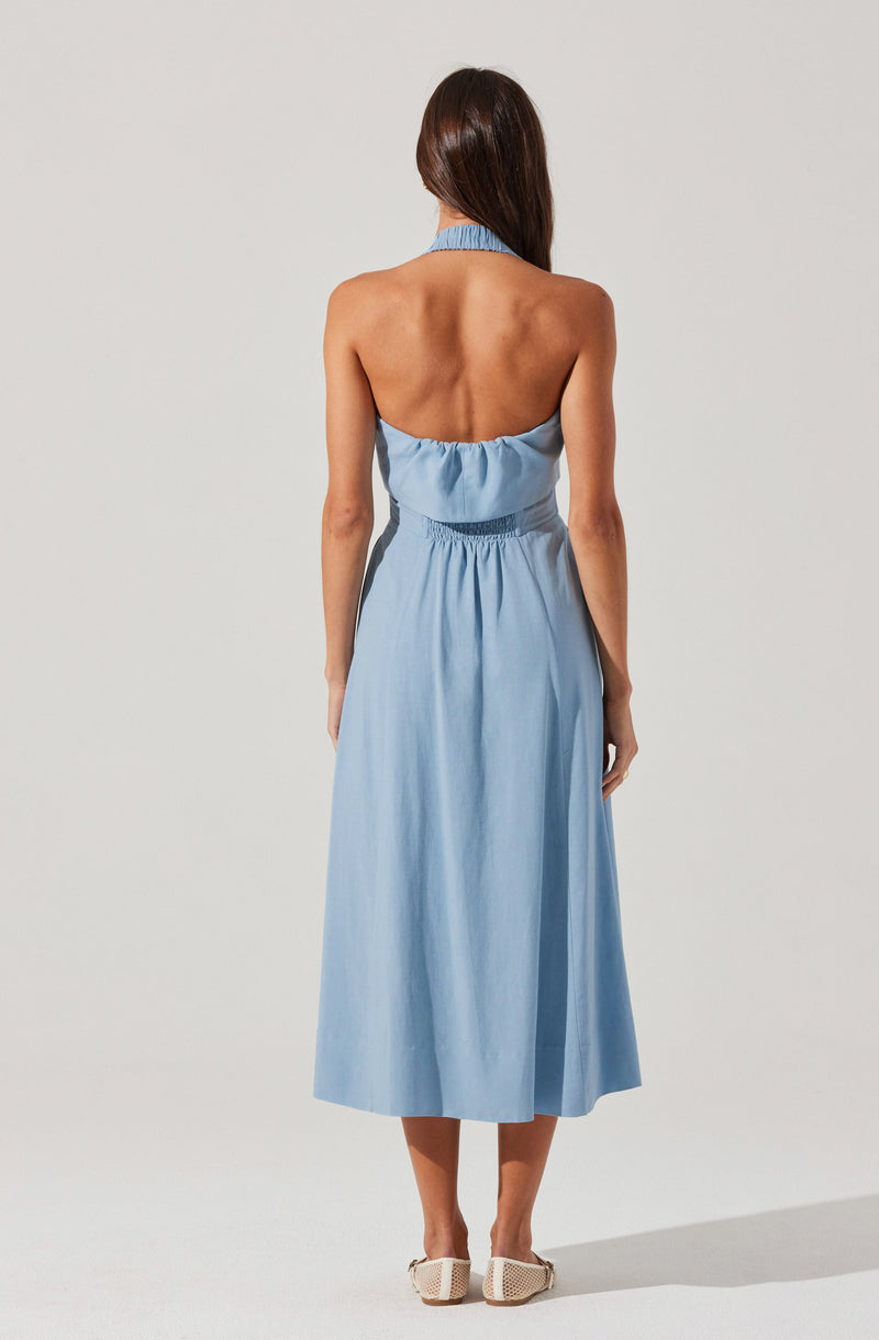 A woman is wearing a sleeveless, halter-neck, light blue dress with a cinched waist. The dress is long, reaching down to her ankles, and has a flowing, relaxed fit. She is also wearing beige, woven, flat shoes.