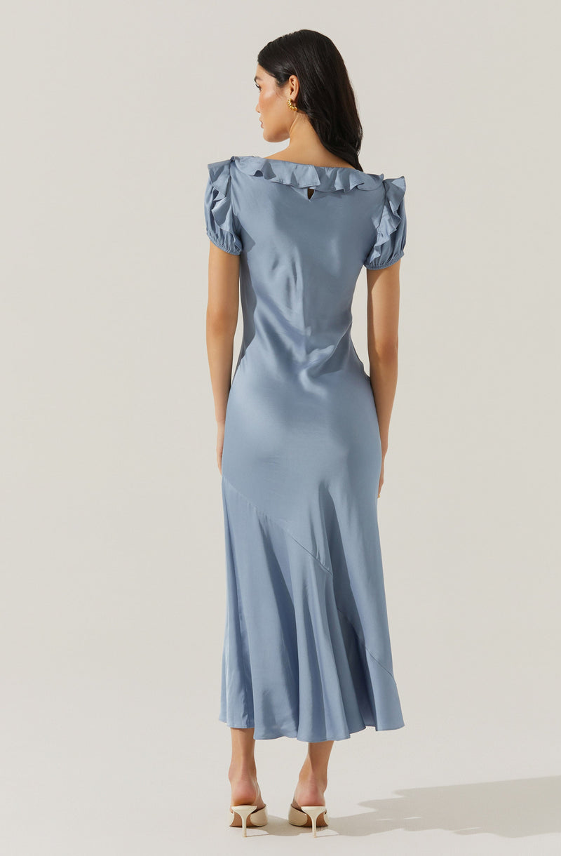 A woman is wearing a long, flowing satin dress in a soft blue color. The dress features puffed short sleeves with ruffle detailing along the shoulder line and a subtle keyhole opening at the back neckline. She has on beige high-heeled shoes.