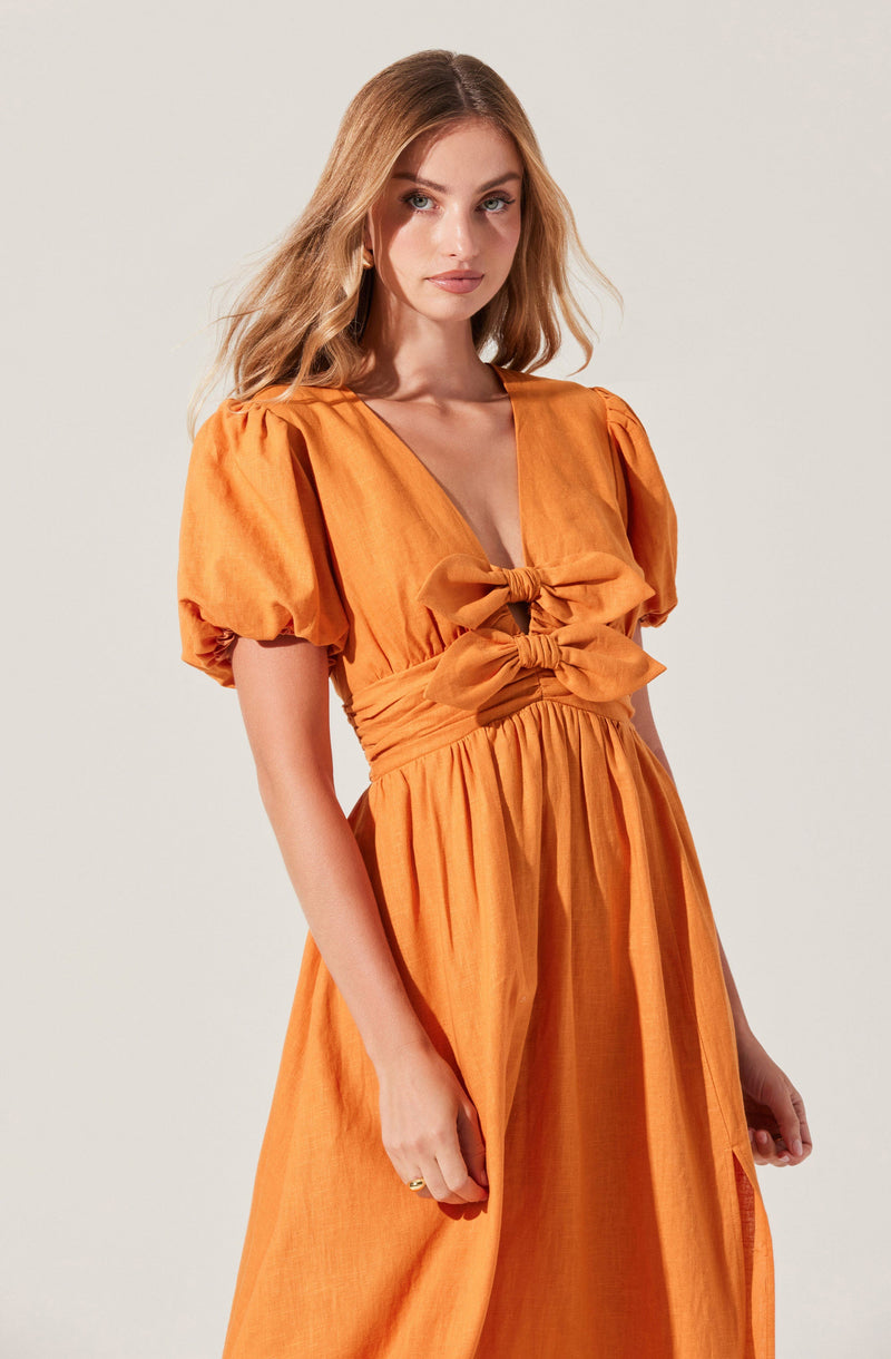 A woman is wearing an orange dress with short, puffed sleeves. The dress features a deep V-neckline and is embellished with two large bows at the waist. The fabric appears lightweight and has a textured, slightly crinkled look.