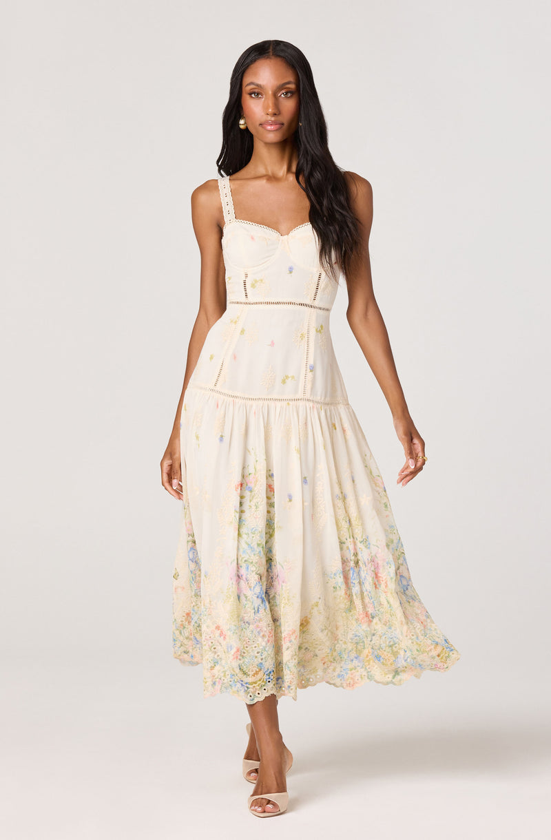 Cream-colored maxi dress with embroidered pastel floral details, sleeveless with wide straps.
