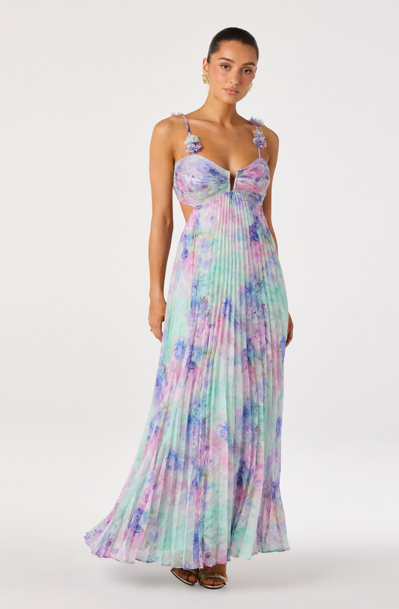 Model wearing a colorful, floral-printed maxi dress with spaghetti straps and floral details on the shoulders.