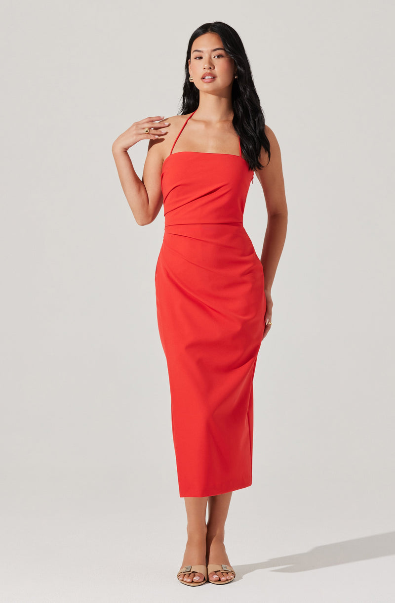 A woman is wearing a sleeveless, fitted, ankle-length dress in a bright red color with thin spaghetti straps. The dress has a straight neckline and a slightly gathered detail at the waist. She is also wearing open-toe heels.