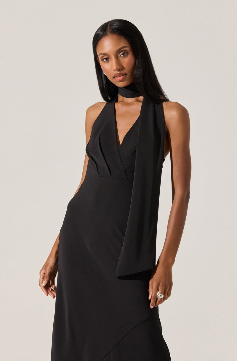A woman is wearing a sleeveless black dress with a deep V neckline. The dress features a long, wide scarf-like tie around her neck that drapes down the front. The fabric appears smooth and slightly shiny.