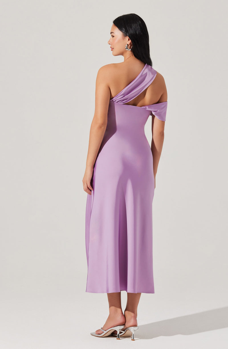 A woman is wearing a lavender-colored satin dress with an asymmetrical, one-shoulder design. The dress features a draped detail over one shoulder, leaving the other shoulder bare, and has a fitted bodice that flows into a wide-leg, calf-length skirt. The fabric has a smooth, shiny appearance, creating an elegant look. She is also wearing open-toe high-heeled shoes with a transparent strap.