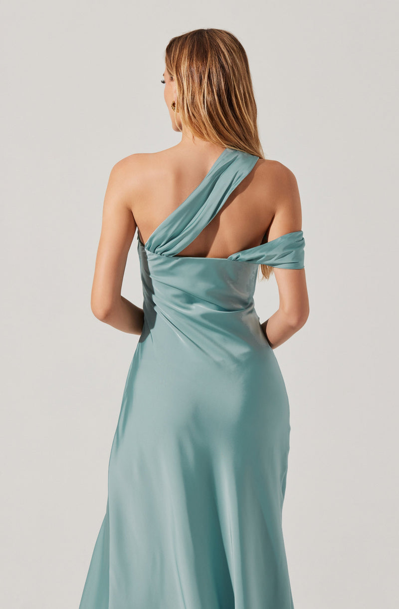 A woman wearing a silky, light blue gown with a draped, one-shoulder design. The gown features an asymmetrical neckline with fabric crossing over her left shoulder and wrapping around her upper arm. The fabric appears smooth and shiny, creating an elegant look.