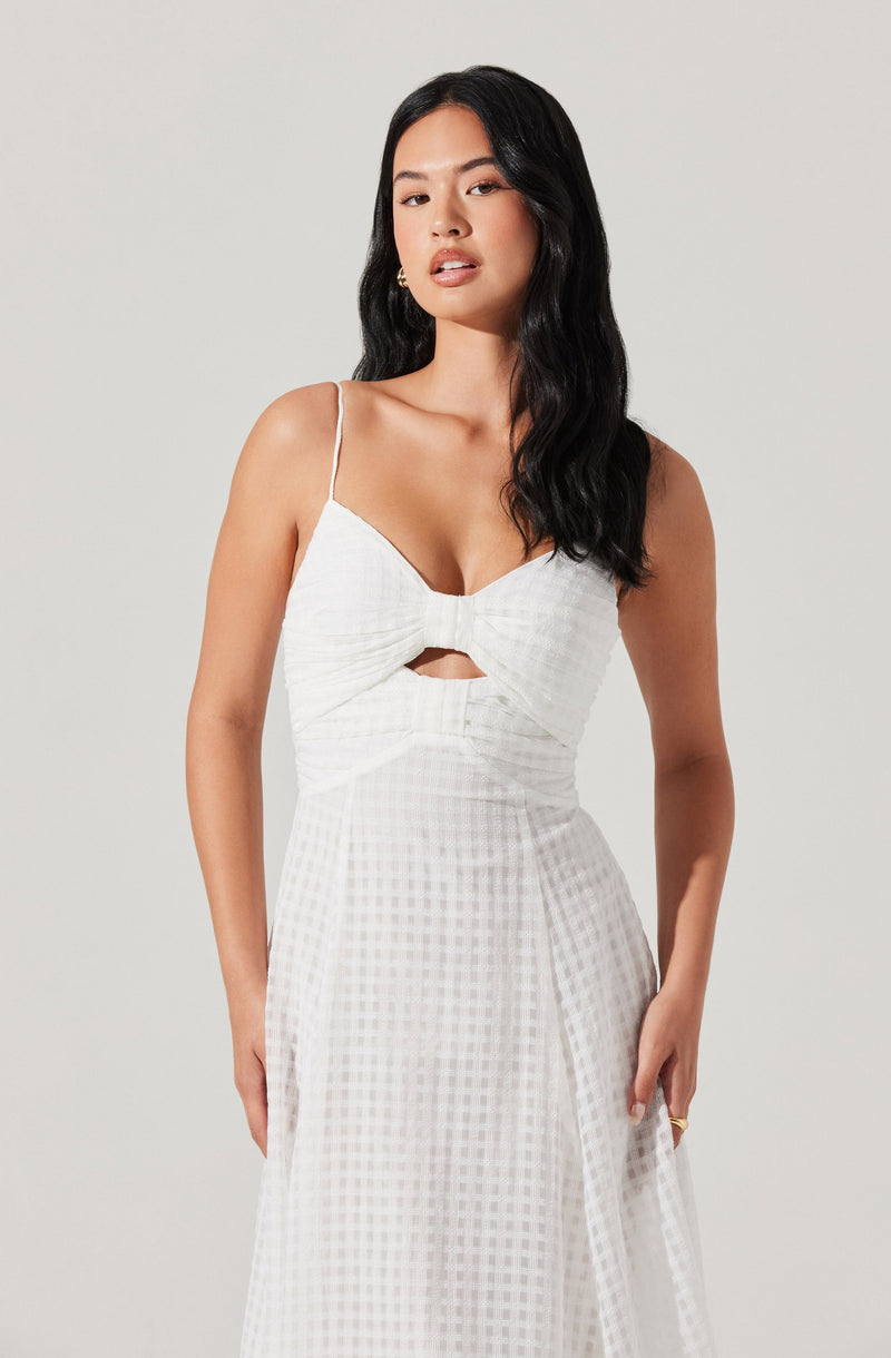 A woman is wearing a white sleeveless dress with thin spaghetti straps. The top part of the dress features a large bow detail in the center and a small cutout below it. The fabric of the dress has a subtle checkered pattern.