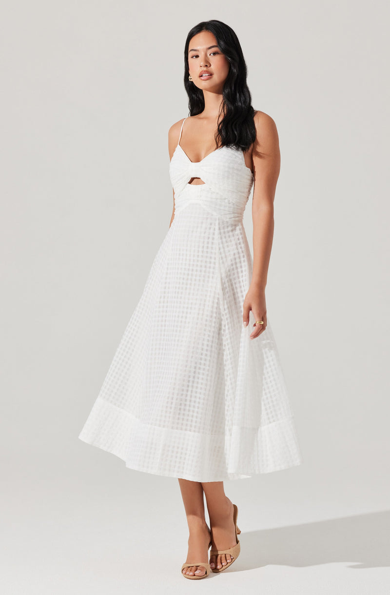 A woman is wearing a white, sleeveless midi dress with thin spaghetti straps. The dress features a fitted bodice with a small keyhole cutout in the center. The skirt is full and has a subtle textured checkered pattern. She is also wearing beige open-toe high heels.