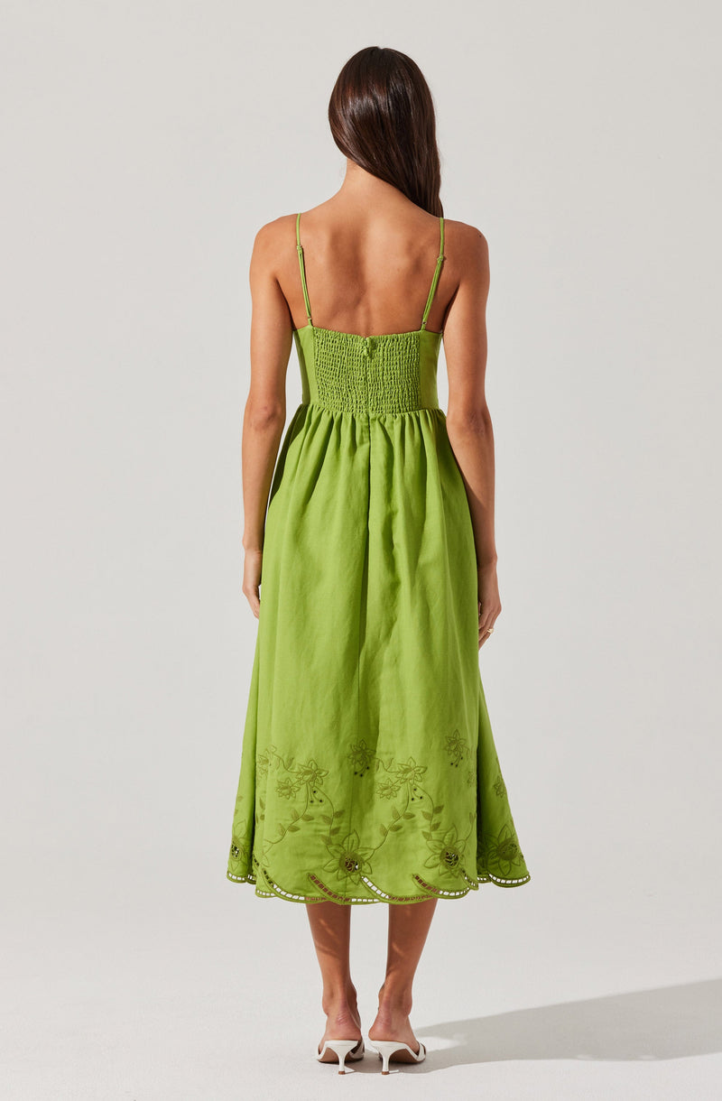 The dress is a bright lime green color with a fitted, smocked bodice and thin spaghetti straps. The skirt is long, flowing, and gathered at the waist, with embroidery detailing along the hem featuring floral and leaf patterns. The fabric appears lightweight and slightly shiny, giving it a summery, elegant look.