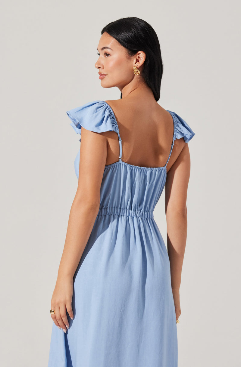A woman is wearing a light blue dress with ruffled short sleeves, a gathered neckline, and an elastic waistband. The dress has thin shoulder straps and is made of a soft, flowy fabric.