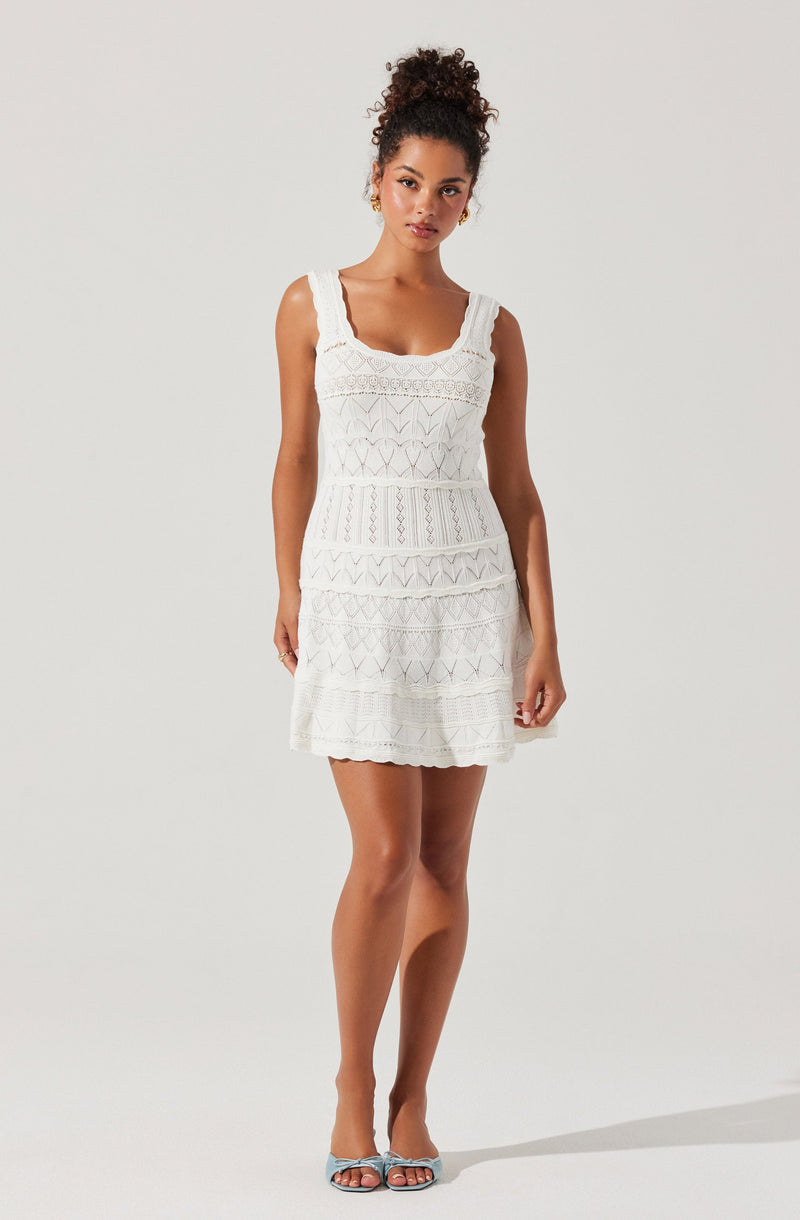 A woman is wearing a sleeveless white dress with a fitted bodice and a slightly flared skirt. The dress features lace and crochet detailing with horizontal patterns throughout. The neckline is square-shaped with wide straps. She is also wearing light blue open-toe sandals with thin straps.