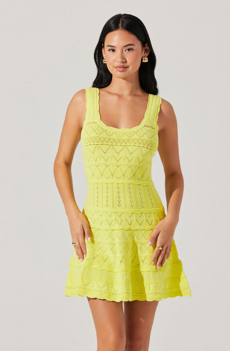 A woman is wearing a sleeveless, bright yellow dress with a fitted bodice and a flared skirt. The dress features intricate, textured embroidery with geometric patterns, vertical and horizontal lines, and scalloped edges. The wide straps also have embroidered detailing, and the dress has a square neckline.