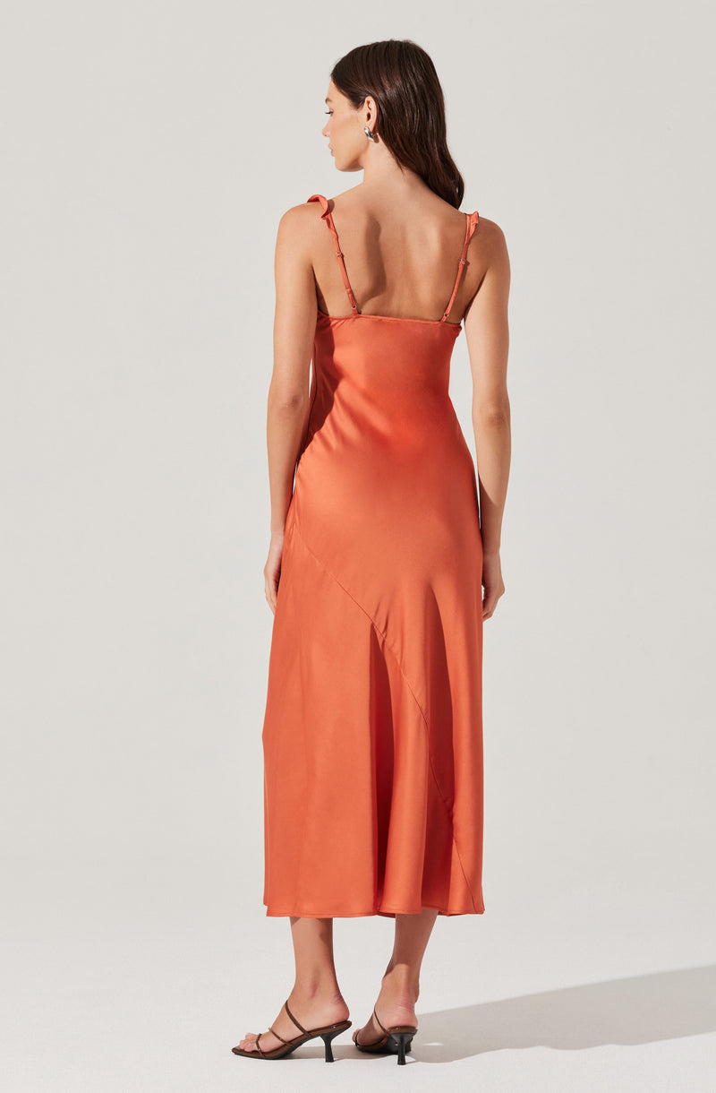 A woman is wearing a flowy, sleeveless, satin midi dress in a warm, burnt orange color. The dress features thin, ruffled shoulder straps and a fitted bodice, falling gracefully to a length mid-calf. She is also wearing open-toe, slip-on high-heeled sandals in a neutral color.