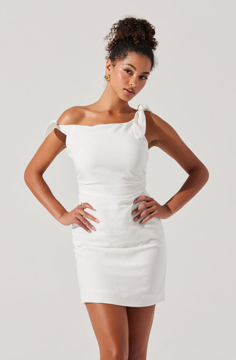 A woman is wearing a white, form-fitting dress that features off-the-shoulder sleeves tied into small bows on each shoulder. The dress is smooth and has a slightly gathered design at the waist.
