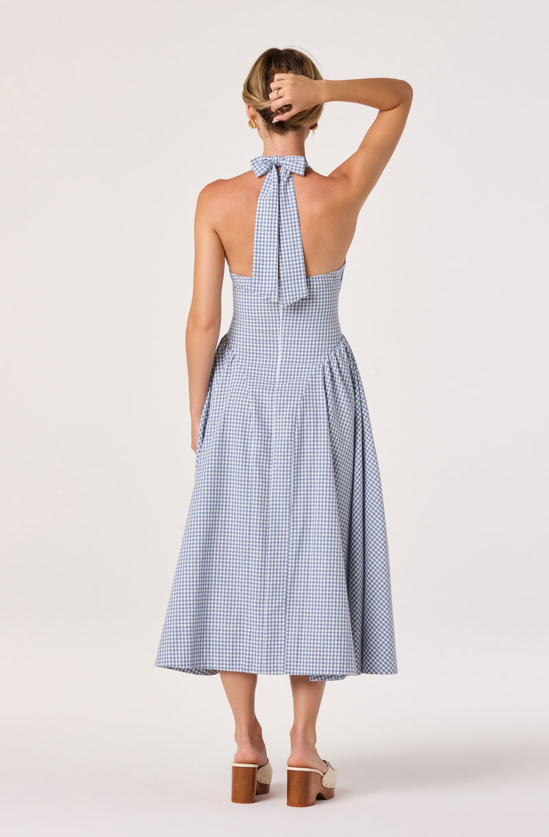 Back view of a woman in a blue and white gingham halter dress with a bow, sleeveless, and ankle length.