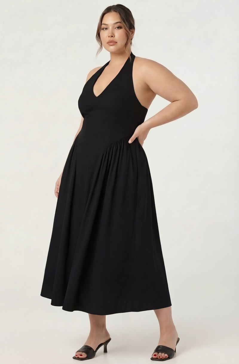 Woman in a sleeveless black halter dress with a pleated skirt, wearing open-toe heels.