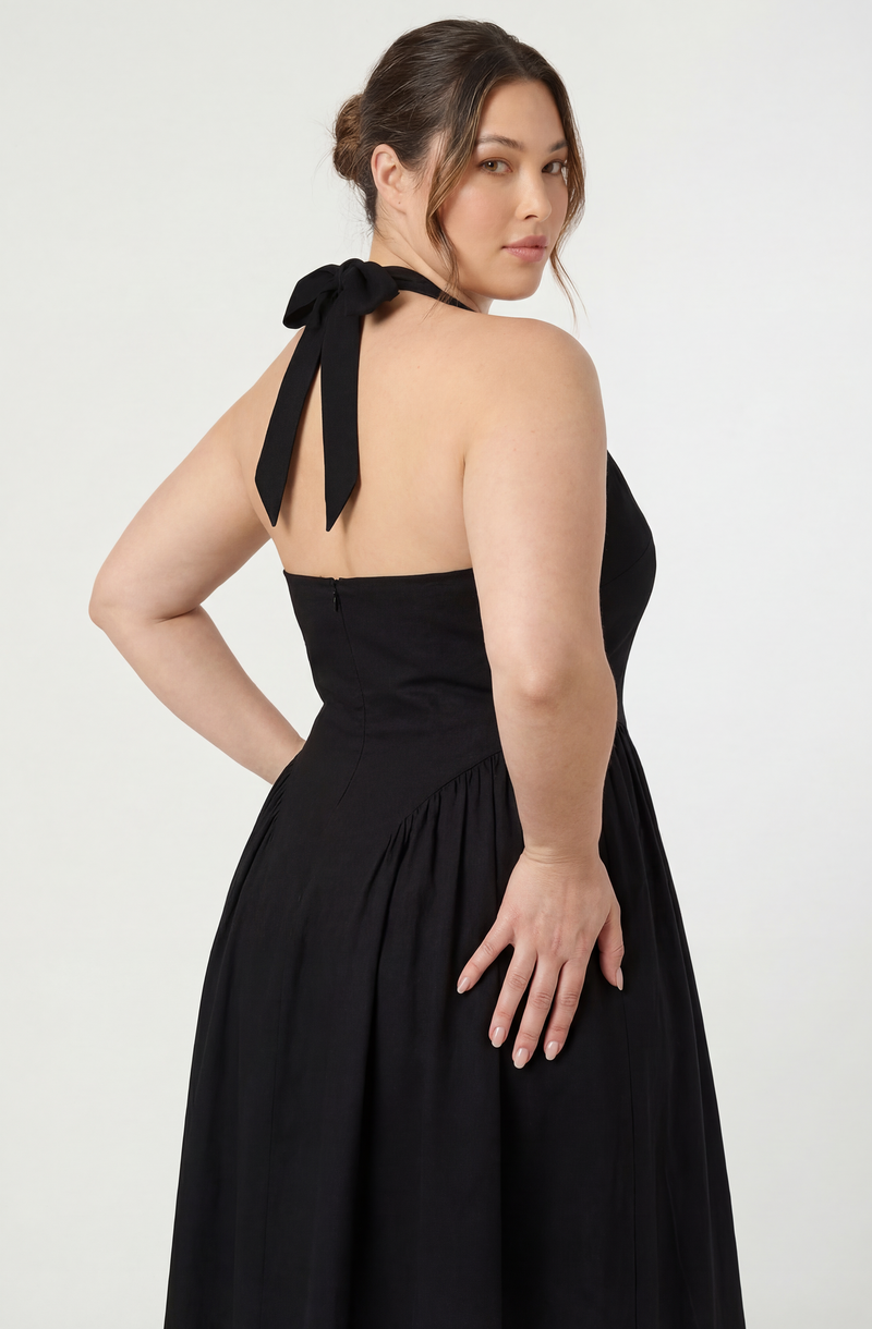 Woman in a black strapless dress with a bow on the shoulder, posing against a plain background.