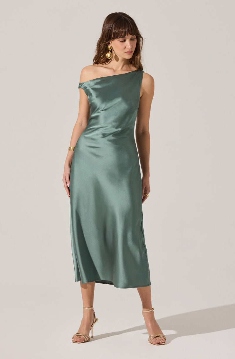 A woman is wearing a long, elegant, satin dress in a muted teal color. The dress has an asymmetrical neckline with one shoulder strap, leaving the other shoulder bare. It is fitted at the waist and flows down to the ankles with a smooth, shiny texture. She pairs the dress with open-toe, high-heeled shoes and large, gold, decorative earrings.