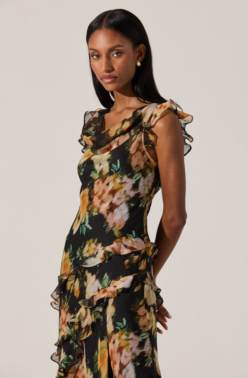 A woman is wearing a sleeveless, fitted dress with a floral print featuring shades of black, green, peach, and cream. The dress has ruffled details along the shoulders and down the sides, adding a textured, layered effect.