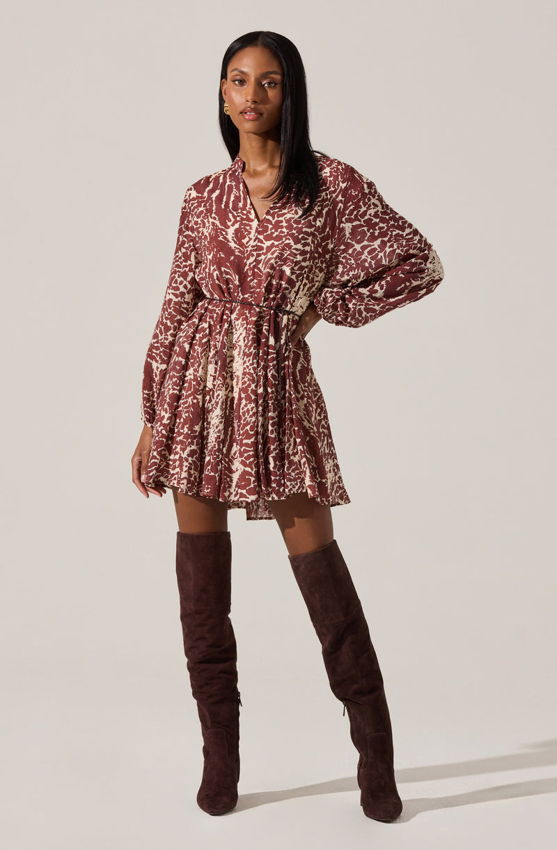 The woman is wearing a long-sleeved, button-up dress with a drawstring waist, featuring a brown and beige animal print pattern. She pairs the dress with tall, dark brown suede over-the-knee boots.