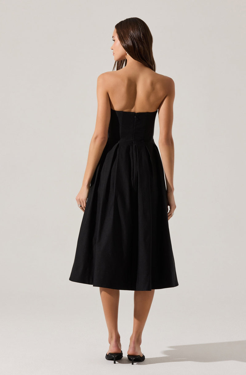 A woman is wearing a strapless black dress with a fitted bodice and a full, midi-length skirt. The dress appears to be made of a smooth, slightly shiny fabric. She is also wearing black open-toe high-heeled shoes.