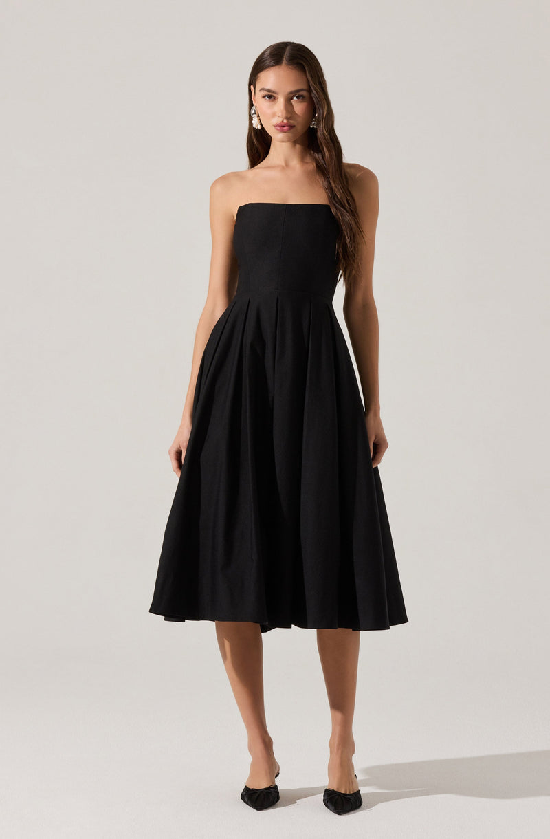 A woman is wearing a strapless, black midi-length dress with a fitted bodice and a full, pleated skirt. She has long, dark hair and is accessorized with large, dangling earrings.