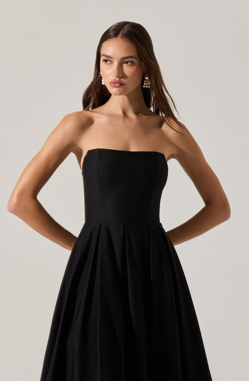 A woman is wearing a strapless black dress with a fitted bodice and a full, pleated skirt. She accessorizes with large, dangling earrings.