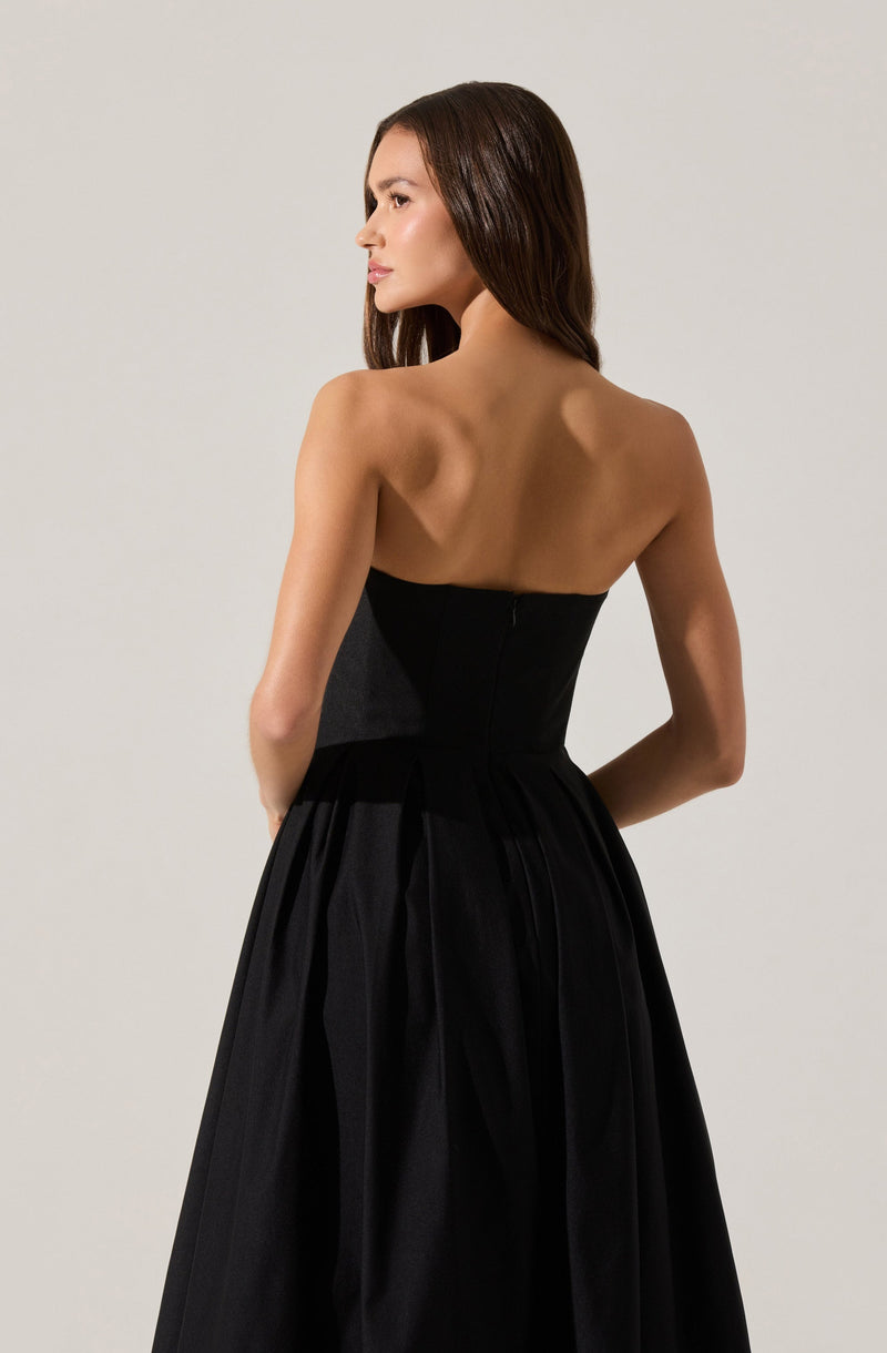 A woman is wearing a strapless, black gown with a fitted bodice and a full, pleated skirt that reaches the floor. The dress appears to be made of a satin or similar shiny fabric, giving it an elegant and sophisticated look.