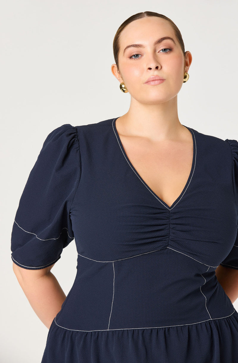 The person is wearing a navy blue dress with a V-neckline, puffed short sleeves, and visible white stitching details outlining the seams and shaping of the garment.